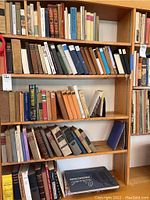 Wider shot of five shelves filled with assorted books in cloth and paper bindings
