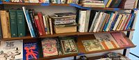Wide front view of bookshelf with assorted books showing titles such as 'Too Many Songs by Tom Lehrer', 'Individuals and Community', and illustrated books.