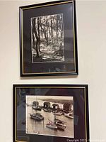 Two framed black and white photographs, one showing a waterfront scene with boats and small structures.