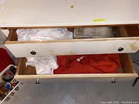 Open wooden drawers with white fabric tablecloths and red runner or cloth inside