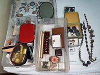 Overview of plastic bins with assorted beads, small boxes, buttons, and trinkets with partially visible embroidered fabric and small mirror