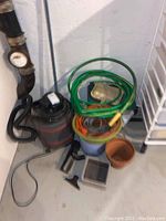 Shop vac with attached hose, extension cord coiled on top, wooden box and flower pots arranged nearby