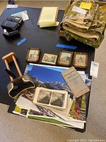 Photo of a vintage wooden stereo viewer, a box labeled Universal View Company containing stereo cards, several small framed architectural prints, a flip desk calendar and folded cloth item.