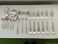 Full overview of 19 pieces laid flat showing spoons, forks, sugar tong, shell dish and rattle
