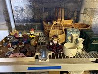 Overview photo showing a selection of Belleek bone china vases and bowl, three wicker baskets, figurines, stained glass sailboat, tins, and a doll arranged on a metal shelving unit.
