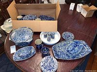 Full set of blue and white speckled Bennington stoneware items on wooden table, including plates, bowls, cups, saucers, mugs, casserole dish, and shakers, some in cardboard box.