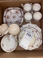 Box with bone china tea set including round floral plates, cups with handles, and saucers, all with gold trim