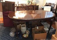 Full view of the oval dining table showing polished cherry wood finish, with the table surrounded by various household items.