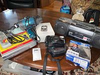View of all electronics items on a wooden table including cameras, DVR, boombox, remote, and cables.