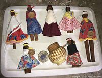 Seven hand carved Latin American indigenous dolls displayed on a white surface with three small woven baskets.