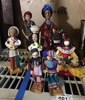 Photo of 9 ethnic dolls including a Frida Kahlo sculpture with colorful traditional dress and other dolls in woven and embroidered attire.