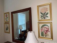 Four floral botanical prints in gold tone frames arranged on a wall near a mirror and lamp