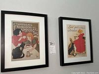 Two black framed vintage advertisement posters side by side on wall, one showing tea and chocolate ad with woman, girl, and cat, other showing milk ad with woman and dog.