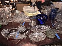 Photo showing various clear cut glass bowls, a cobalt blue bowl, and glass vases on a table.