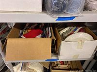 Photo showing two cardboard boxes filled with assorted party supplies including napkins, ribbons, cards, and paper plates.