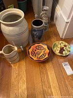 Entire lot arranged on hardwood floor showing all 5 items: 3 pitchers, 1 footed bowl, 1 decorative plate.
