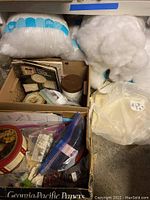 Box with two large bags of white polyester stuffing, along with cardboard boxes containing other sewing supplies and a plastic bag with fabric.