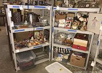 Two plastic shelving units in a basement filled with items; shelving units have four shelves, white with gray supports, dusty and dirty.