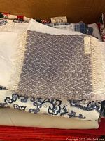Photo showing various folded table linens stacked in box including the gray woven place mat on top