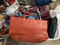 Photo showing a pile of six leather handbags in various colors and styles, including a large orange Nine West tote on top.