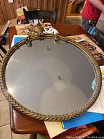 Front view of circular mirror showing gold gilded frame and part of the mirrored surface.