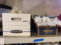 Two boxes containing vintage textiles and clothing items on a basement shelf