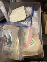 Plastic bins and bags containing assorted vintage linens, napkins, and handkerchiefs.
