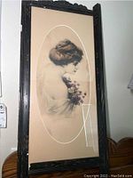 Full view of the framed antique print showing the woman holding violets in an oval mat within a black wooden frame with chips.