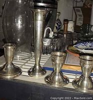 Four weighted sterling silver items on a tiled surface including three candlesticks and a bud vase showing overall form and condition.