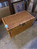 Full view of rectangular wicker chest on concrete floor in basement, showing entire chest with lid closed.