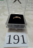 Ring seated in clear acrylic display box on fabric background with lot number card