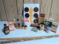 Overview of the vintage advertising items including yardsticks, bottles, tins, boxes, and Filter Queen coasters with spoons arranged on a table against wood paneling.