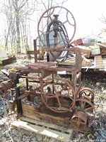 Full view of old rusty bandsaw with large metal spoked wheels and wooden base outdoors.