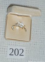 Brooch shown at an angle inside beige jewelry box on cream colored fabric base.