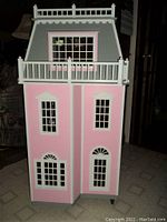 Front exterior view of pink and gray dollhouse with white railings and multiple windows