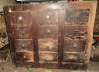 Front view of the old wood chest showing all 12 drawers arranged in three columns with several handles missing and worn wood surface.