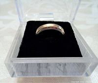 Ring displayed in clear plastic box on black cushion, front view