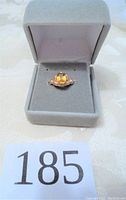 Overall view of gold ring with yellow gemstone in a jewelry box.