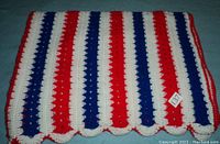 Close-up of folded afghan showing red, white, and blue vertical stripes and scalloped edge