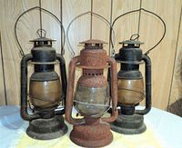 Vintage GSW lanterns in black metal with one heavily rusted lantern center with cracked glass globe. All have wire hangers and fuel caps visible at base.