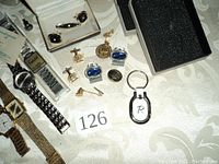Photo showing lot with watches, cuff links, buttons, tie clips and key ring arranged on tablecloth.