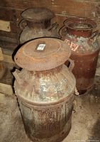 Three old rusty milk cans grouped with visible rust and wear, one missing lid.