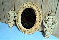 Photo showing vintage oval mirror with detailed cream ornate frame and two matching candle sconces on each side against a wood paneled background