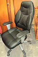 Side view of black office chair showing padded contoured seat and backrest with armrests and caster wheels.
