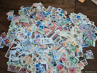 Photo showing a large pile of used U.S. postage stamps of various denominations and designs spread on a wooden surface.