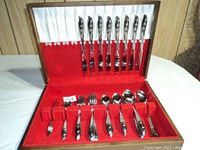 Photo showing the set of stainless silver-setting flatware inside a wooden case with red velvet lining. Includes knives secured in the lid, various spoons, forks, and specialty utensils in the base.