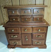 Front view of the larger wooden jewelry box showing six small drawers on top, six drawers and a central door below with decorative metal knobs and handles.