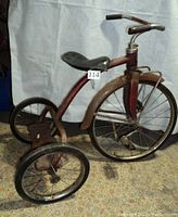 Side view showing large 20 in front wheel, rusty metal frame, black seat, and rear wheels.