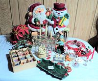 Photo showing the full assortment of Christmas decorations including the large Santa and snowman figures, boxed ornaments, glasses, music box, and assorted small items spread on a table.