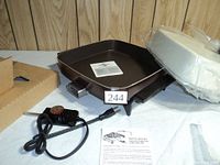 Square brown electric fry pan base with handles, detachable power cord with temperature control knob, white lid wrapped in plastic, instruction sheet beside, original packaging box open.